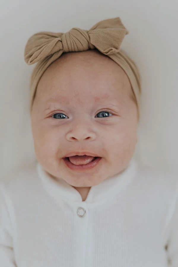 Licensed stock photo used for fictional Mila: a smiling baby wearing a beige bow and white outfit.