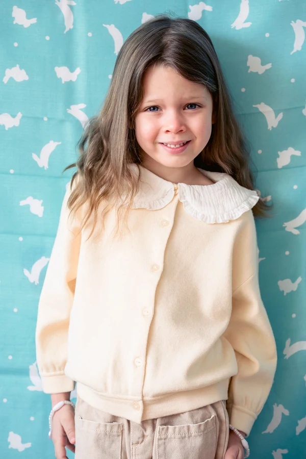 Licensed stock photo used for fictional Tess: a smiling child with long brown hair and a cream cardigan.